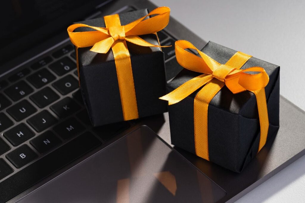 Two small black gift boxes tied with bright yellow ribbons resting on a dark laptop