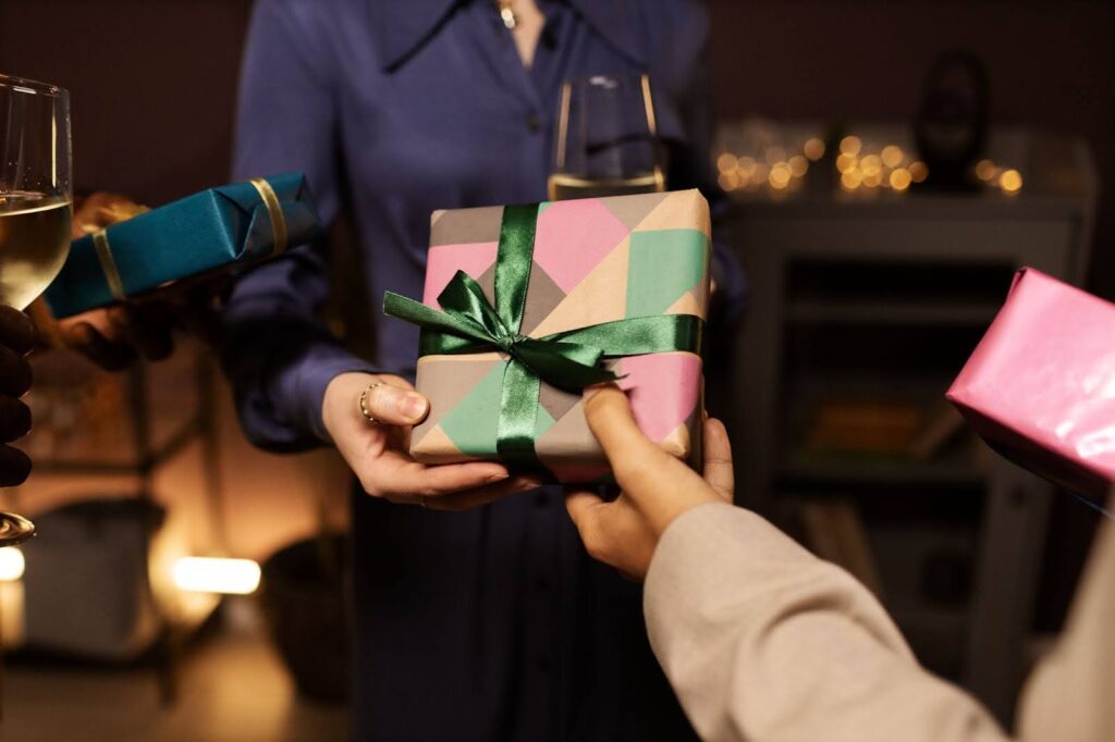 Close-up of two people's hands exchanging a present wrapped in colorful geometric paper and tied with a green satin ribbon.